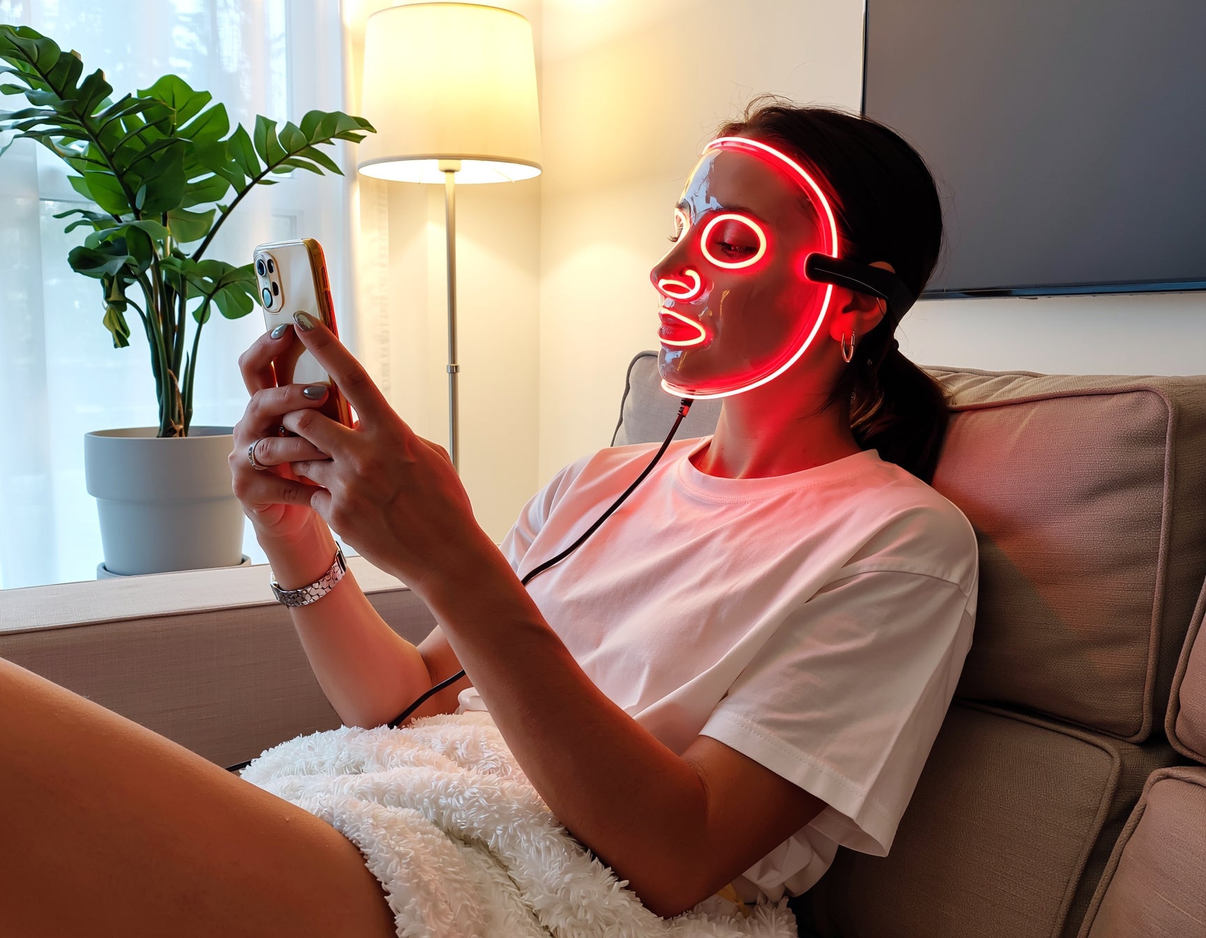 Persoon die thuis ontspannen een roodlichttherapie masker gebruikt in een rustige moderne woonkamer.